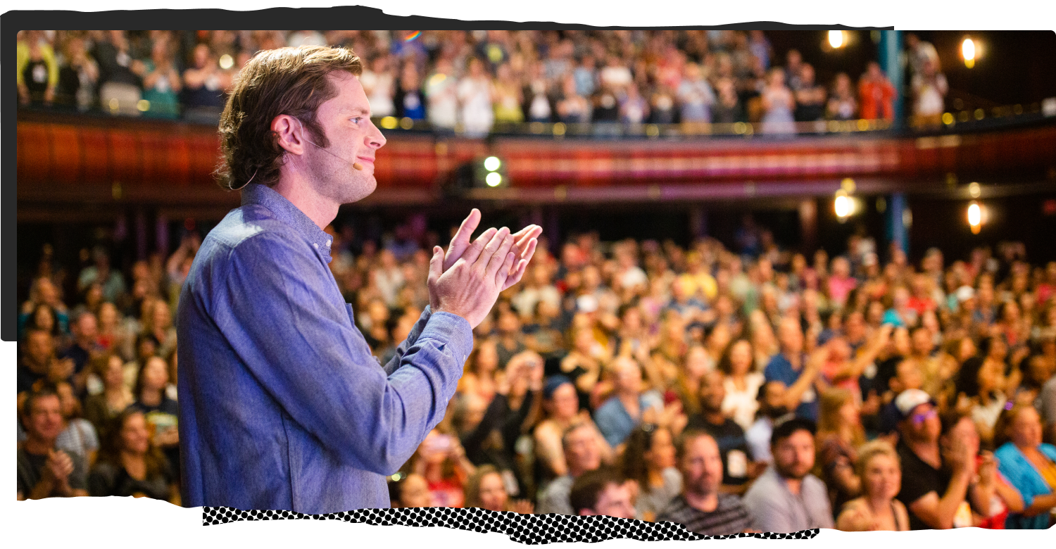 Chris Guillebeau on stage in front of a large applauding audience